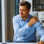 Office worker experiencing shoulder pain while sitting at desk computer workstation