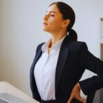 Woman doing lower back pain relief stretch at office desk for workplace wellness